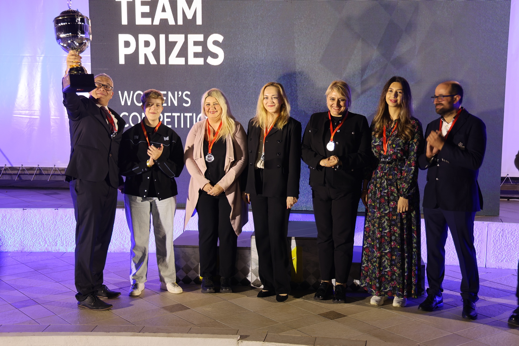 Club president Jan Bednarich raises the trophy as Gambit Bonnevoie’s women and coach celebrate their European silver medals on stage in Budva.